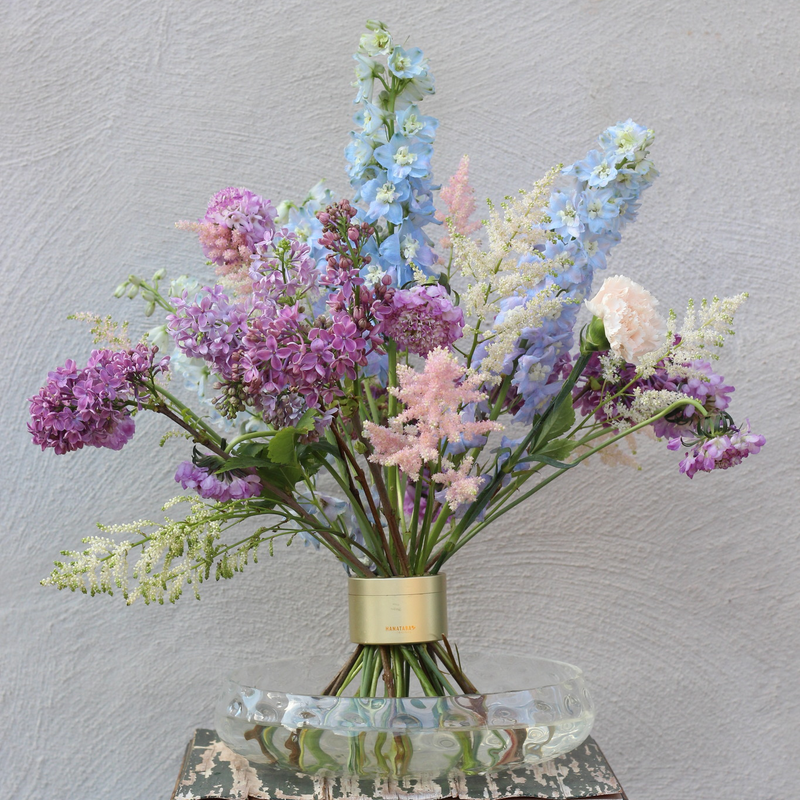 Elegant Ikebana bloemstuk met een verscheidenheid aan pastelkleurige bloemen, waaronder seringen en ridderspoor, vastgezet door een chique Spiral Stem houder.