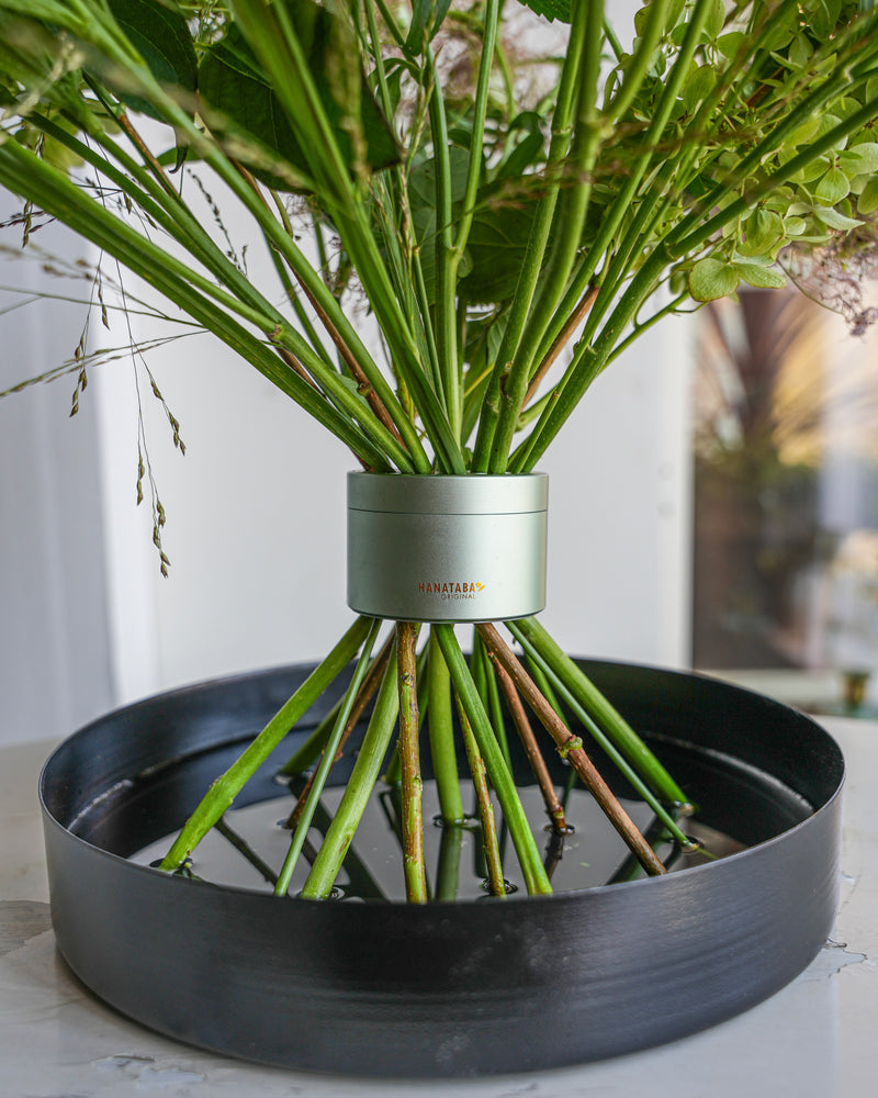 Bloemstelen in een weelderig Ikebana boeket op een zwarte bloementray gevuld met water.