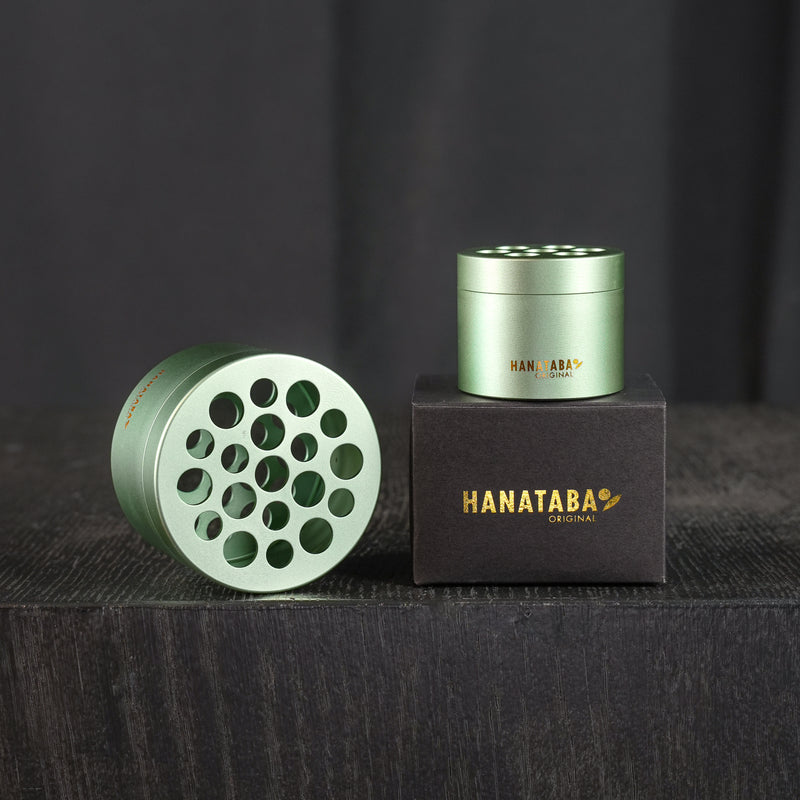 Twee Hanataba boeket twisters in het Matcha Green ontwerp. De producten staan in de originele zwarte verpakking met Hanataba Original in goud geschreven. De producten staan in een donkere kamer op een zwarte houten tafel.