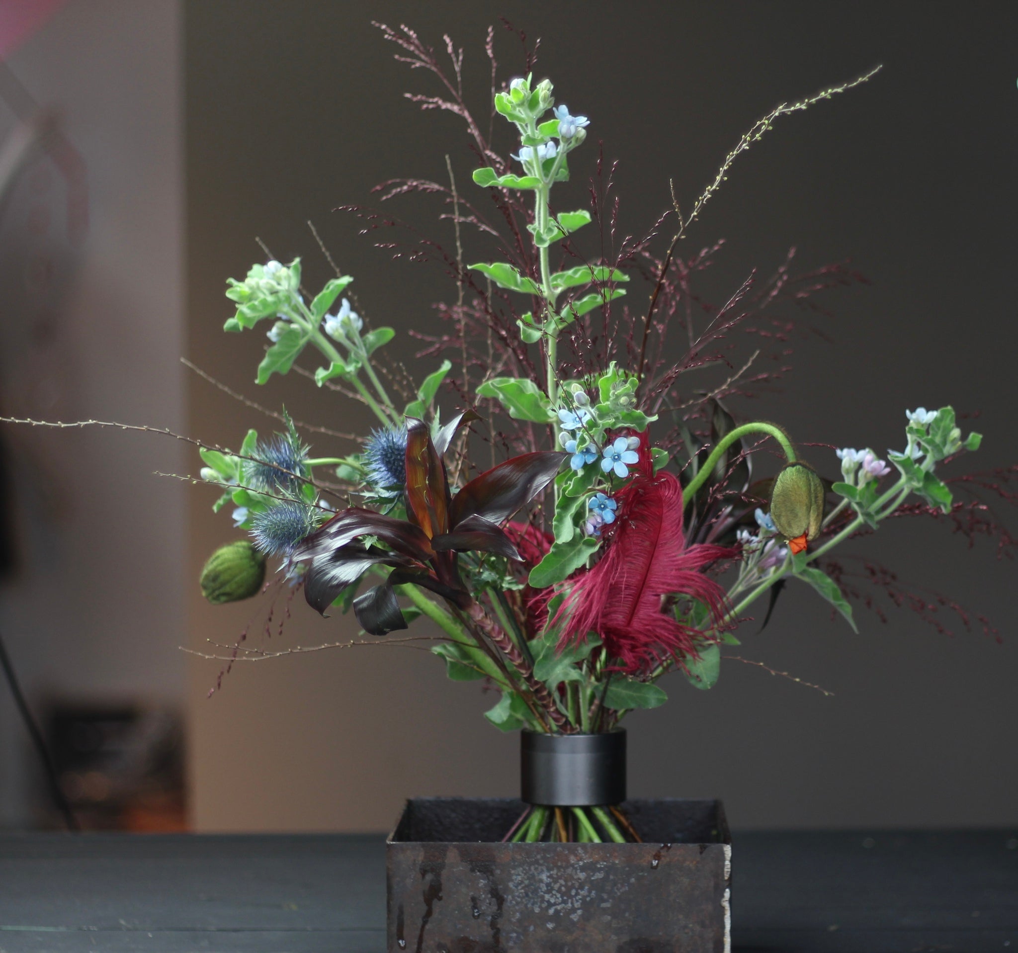 Ikebana arrangement met een verscheidenheid aan bloemen en gebladerte, vastgezet met een Hanataba pikzwarte spiraalvormige steelhouder.