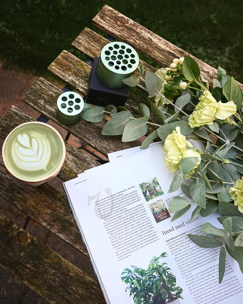 Eucalyptus en een kopje matcha thee naast het Hanataba boeketdraaiapparaat op een houten tafel in een tuin.