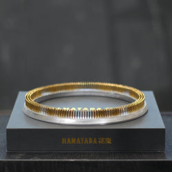 Een glanzende 200 mm Kenzan ring rust op een slanke grijze presentatiedoos met de gouden inscriptie "HANATABA 花束," een toonbeeld van elegantie en functionaliteit in bloemschikken.