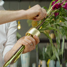 De handen van een man monteren vakkundig een levendig bloemstuk met behulp van een Hanataba Champagne Gold.