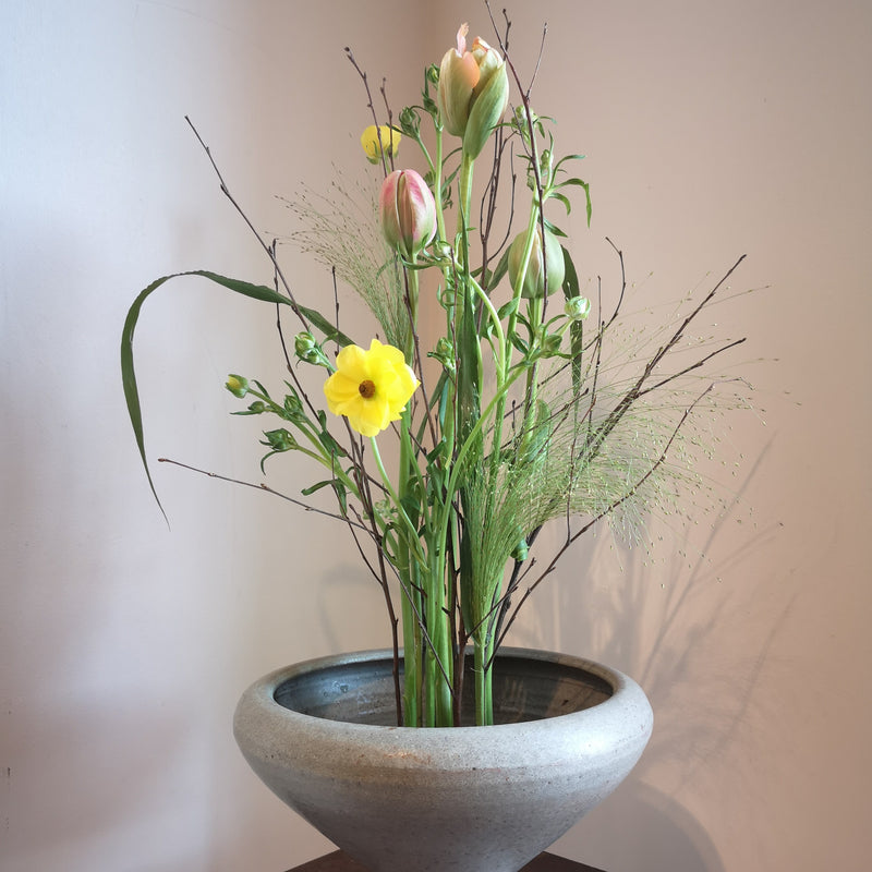  Een serene bloemenpresentatie met een gele narcis en zachtroze tulpen, allemaal vastgezet met een 70 mm Kenzan ring in een stenen schaal.